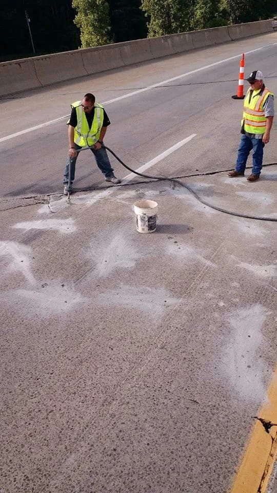 Two workers repairing a roadway with safety gear.